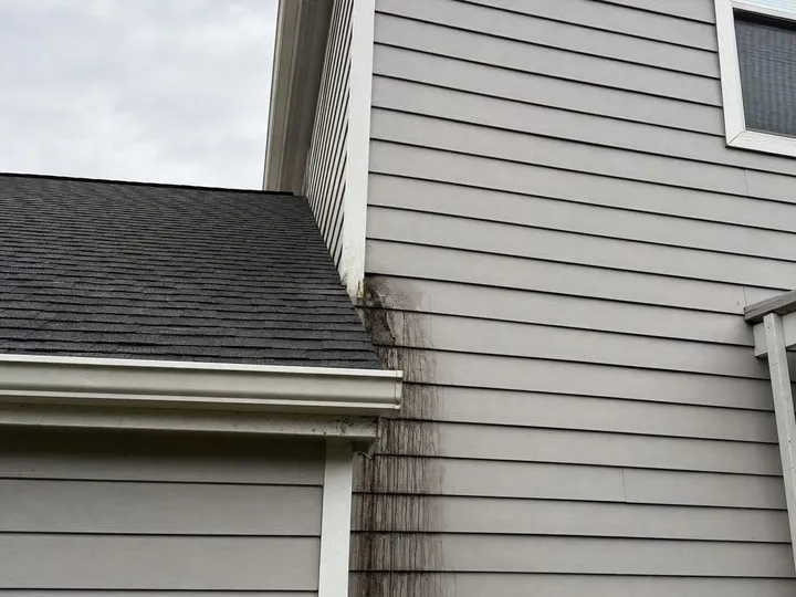 Dark water stains running down lap siding below the point where a garage roof meets a two-story wall